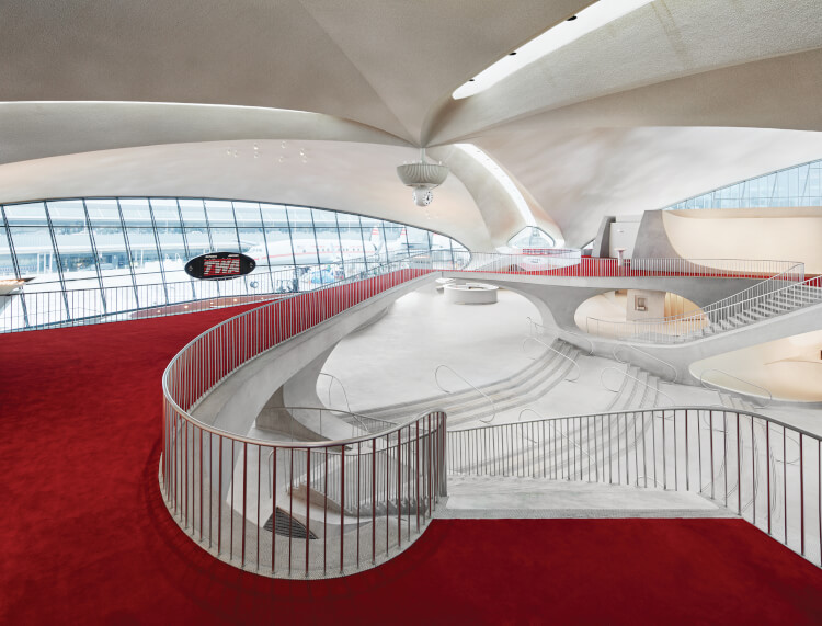 The lobby of the TWA terminal has a red carpet and sweeping curves in the ceiling and bannisters
