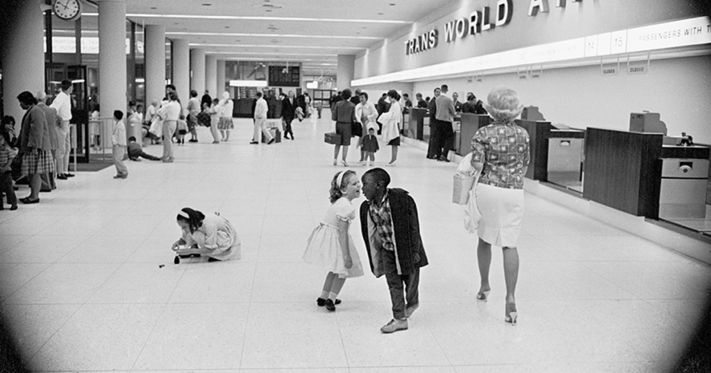 Two children, one black and one white, play in an airport terminal in the 1960s