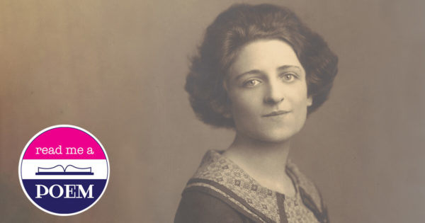 A brunette woman in 1920s attire looks directly at the camera