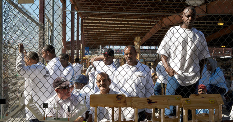 Men standing in a prison yard behind a chain-link fence