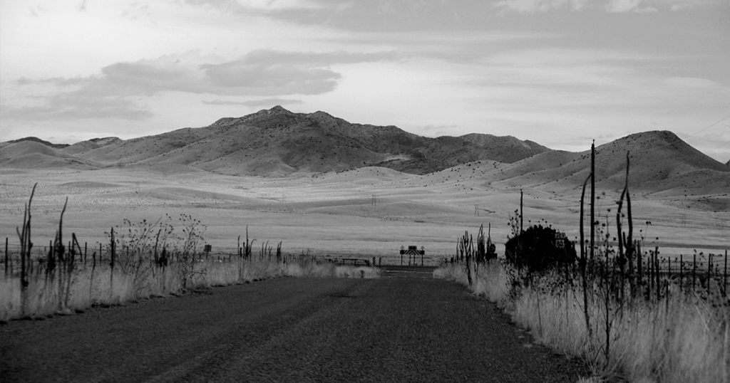 Black and white shot of a dirt road reading to open desert hills