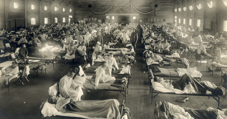 Sepia-toned image of army trainees ill with influenza on twin-sized cots in a large, crowded room. Doctors and nurses sit or stand nearby.