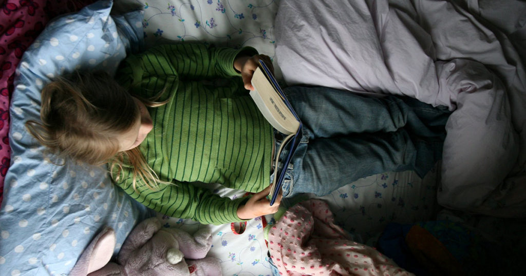 A young child in a green sweater lying in bed with a book and stuffed bunny