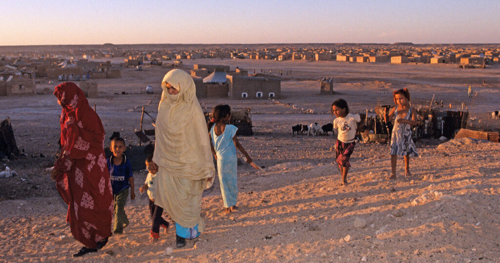 Cloaked women and children walking through the desert at sunset