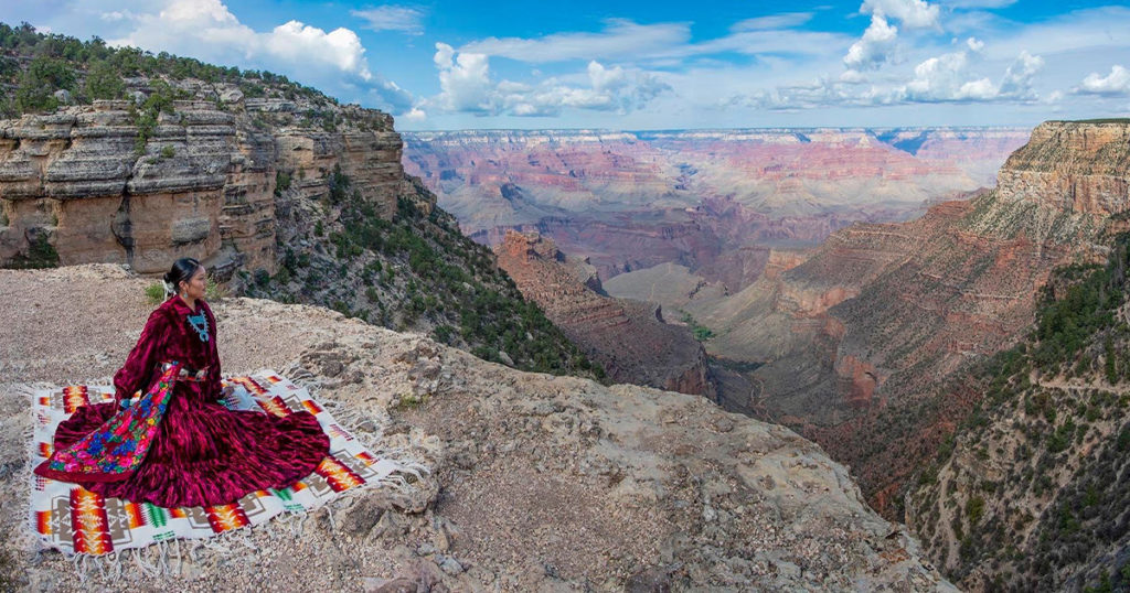 A Diné woman in traditional dress on the rim of the Grand Canyon (Grand Canyon NPS/Flickr)