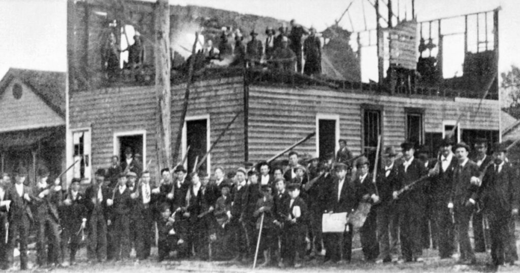 Armed militiamen pose in front of the burned-down headquarters of the <em>Daily Record,</em> Wilmington's only Black newspaper, following the November 1898 massacre (Wikimedia Commons)